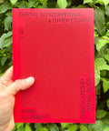 A hand holds a bright red book titled 'Digital Schizophrenia & Other Essays' by Anne Alombert, with green foliage in the background.