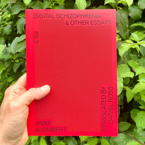 A hand holds a bright red book titled 'Digital Schizophrenia & Other Essays' by Anne Alombert, with green foliage in the background.