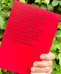 A hand holds a bright red book or booklet in front of green foliage. The cover features black text that reads, 'IT IS NO LONGER POSSIBLE TO CONSIDER DIGITAL TECHNOLOGIES MERELY AS TOOLS THAT ONE MIGHT USE WELL OR BADLY; RATHER, THEY CONSTITUTE OUR DAILY ENVIRONMENTS, AND THESE ENVIRONMENTS ARE CONSTANTLY TRANSFORMING US.